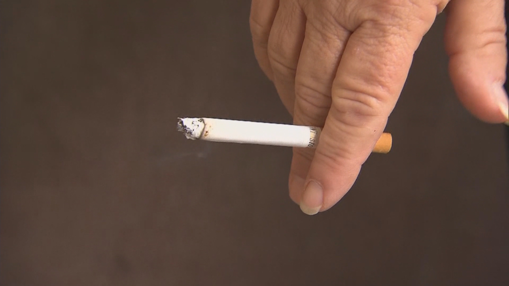 Hands rolling a cigarette using loose tobacco from a 30g pouch with filters and papers laid out on a wooden table