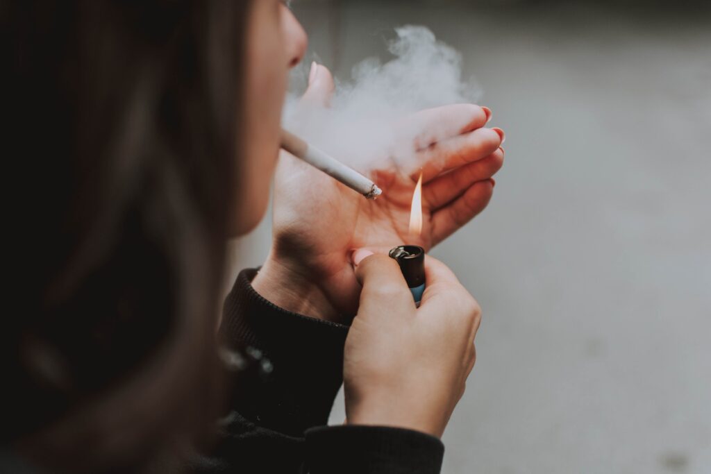 A person holding a cigarette outdoors while exhaling smoke, representing the question of why people do smoke.